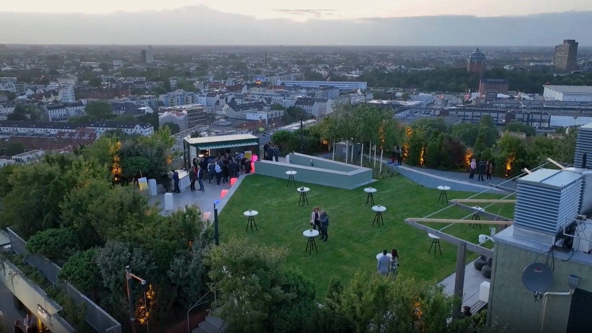 a group of people standing around a green lawn with tables and chairs